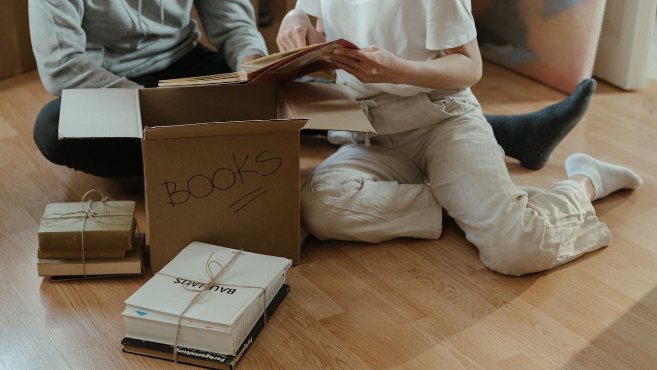 Zwei Personen packen beim Umzug Bücher in einen Karton.