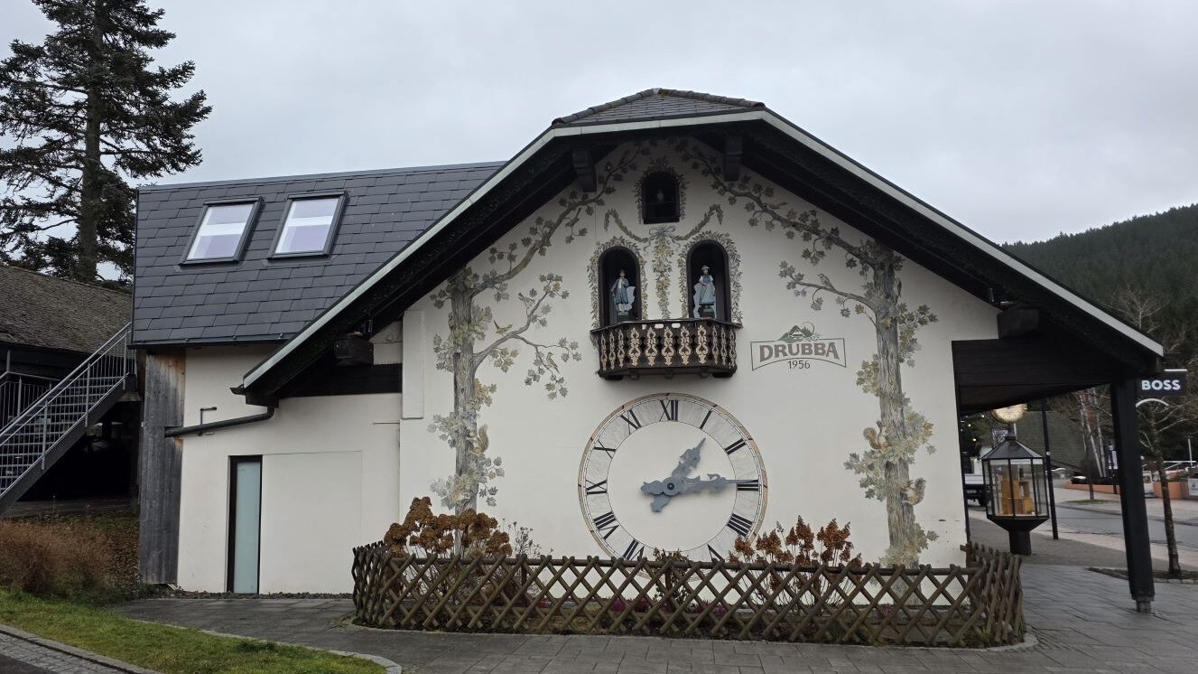 Haus mit einer großen Kuckucksuhr an der Fassade und einem Balkon mit Figuren