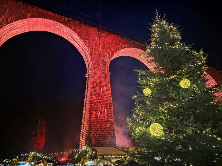 Weihnachtsmarkt in der Ravennaschlucht (08.12.2025) Roter Eisenbahnviadukt des Weihnachtsmarkt in der Ravennaschlucht bei Nacht. Weihnachtsbaum mit großen Kugeln und Marktstände.