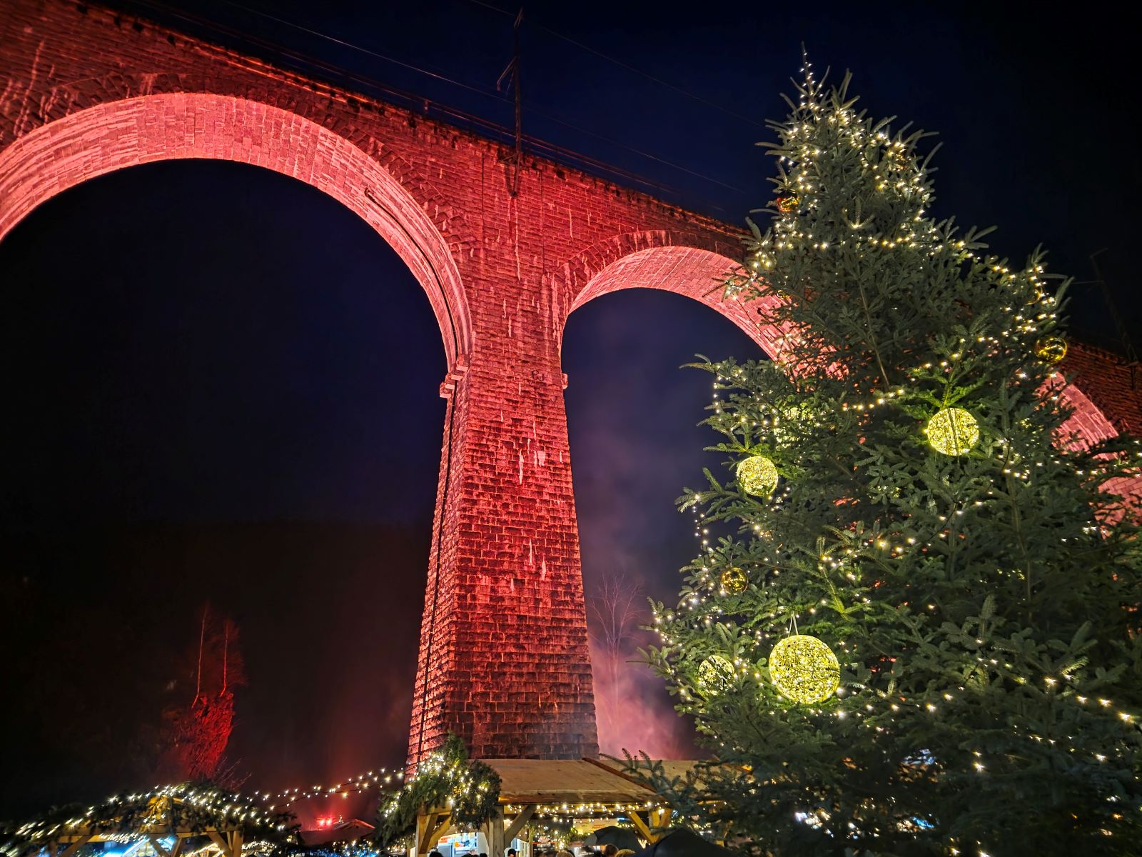 Roter Eisenbahnviadukt des Weihnachtsmarkt in der Ravennaschlucht bei Nacht. Weihnachtsbaum mit großen Kugeln und Marktstände.