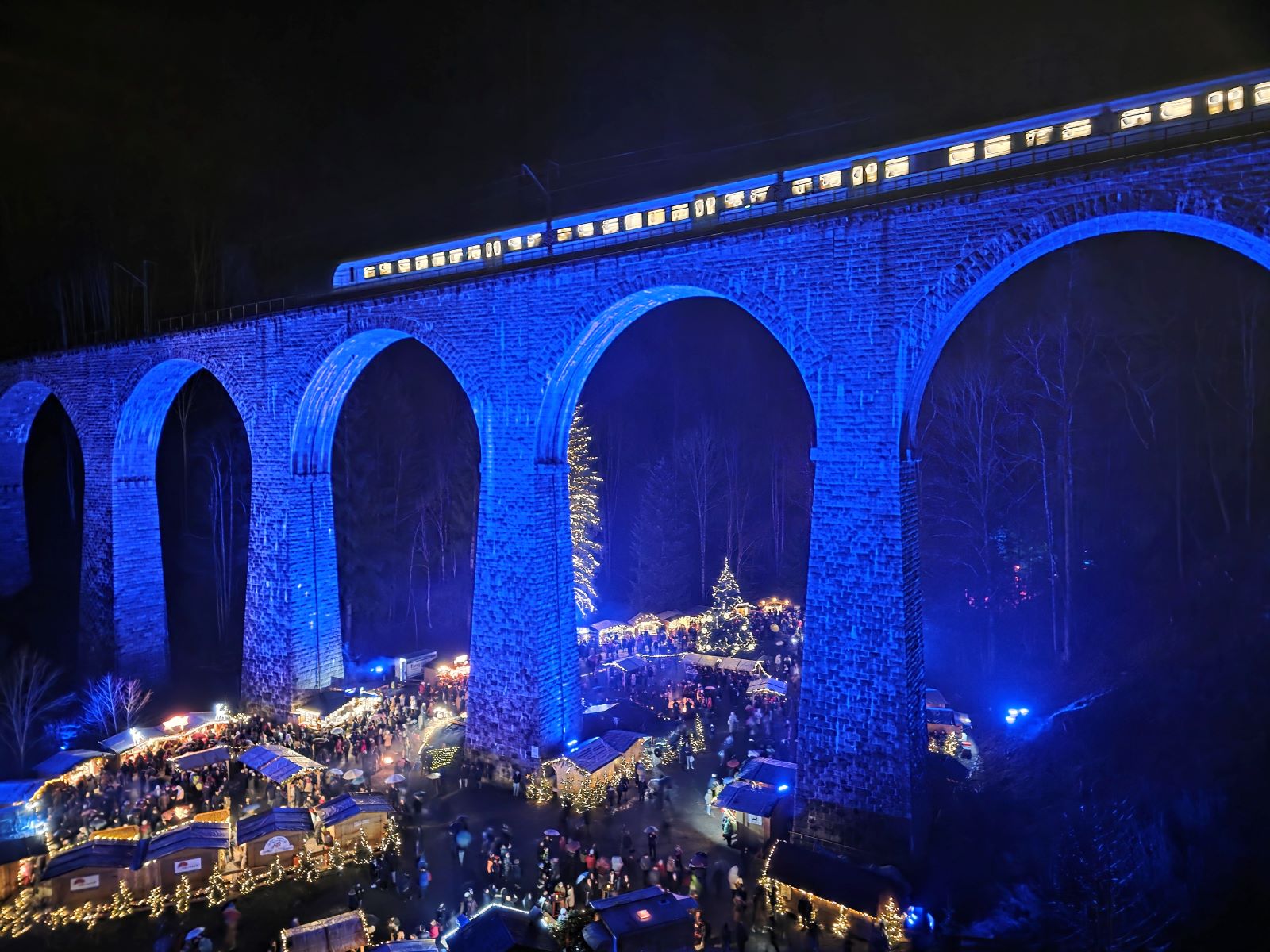 Blau beleuchteter Weihnachtsmarkt Ravennaschlucht bei Nacht. Zug fährt über das Viadukt.