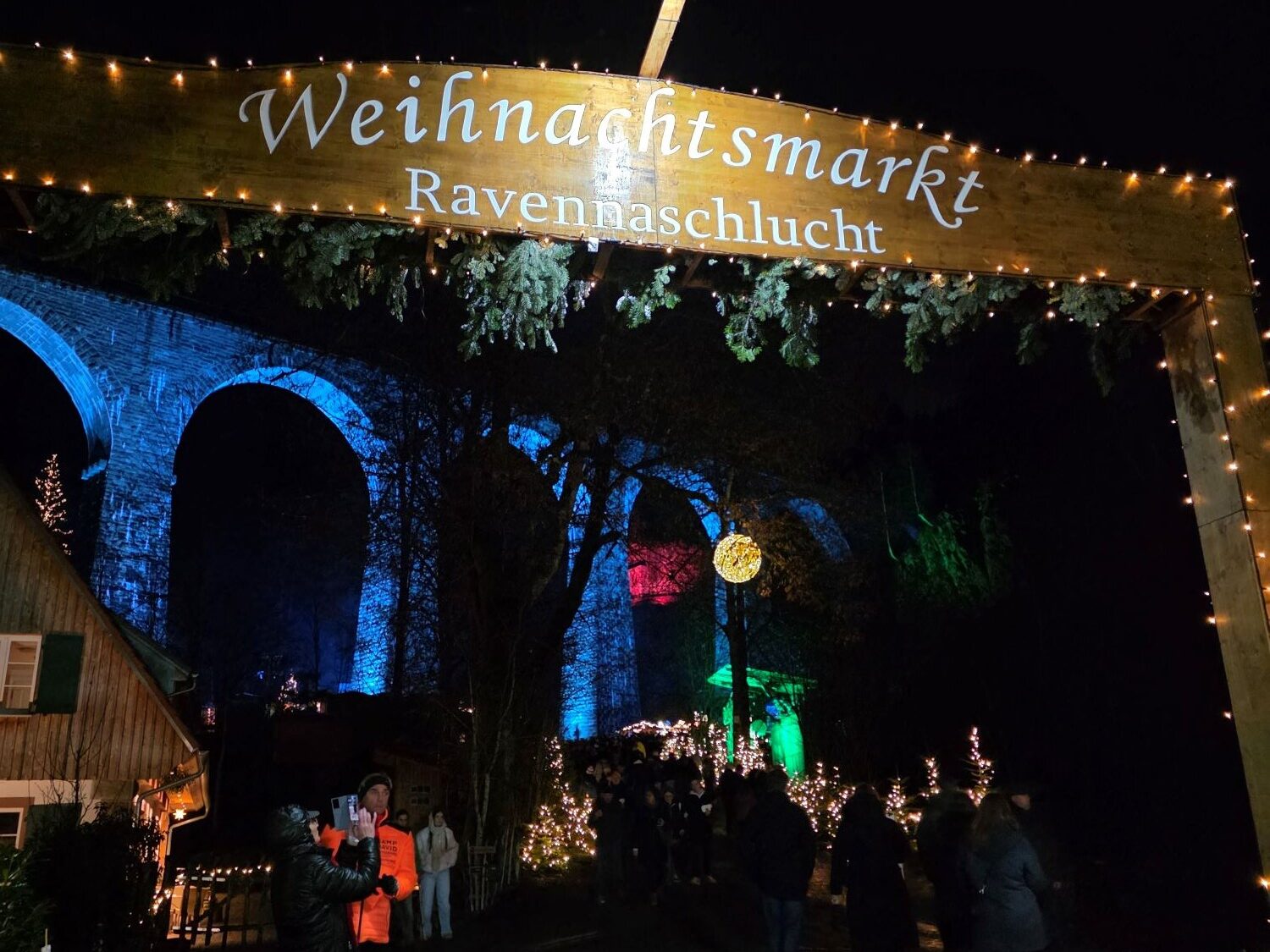 Nachts beleuchteter Eingangsbereich des "Weihnachtsmarkt Ravennaschlucht". Im Hintergrund blau leuchtende Viadukt-Bögen.
