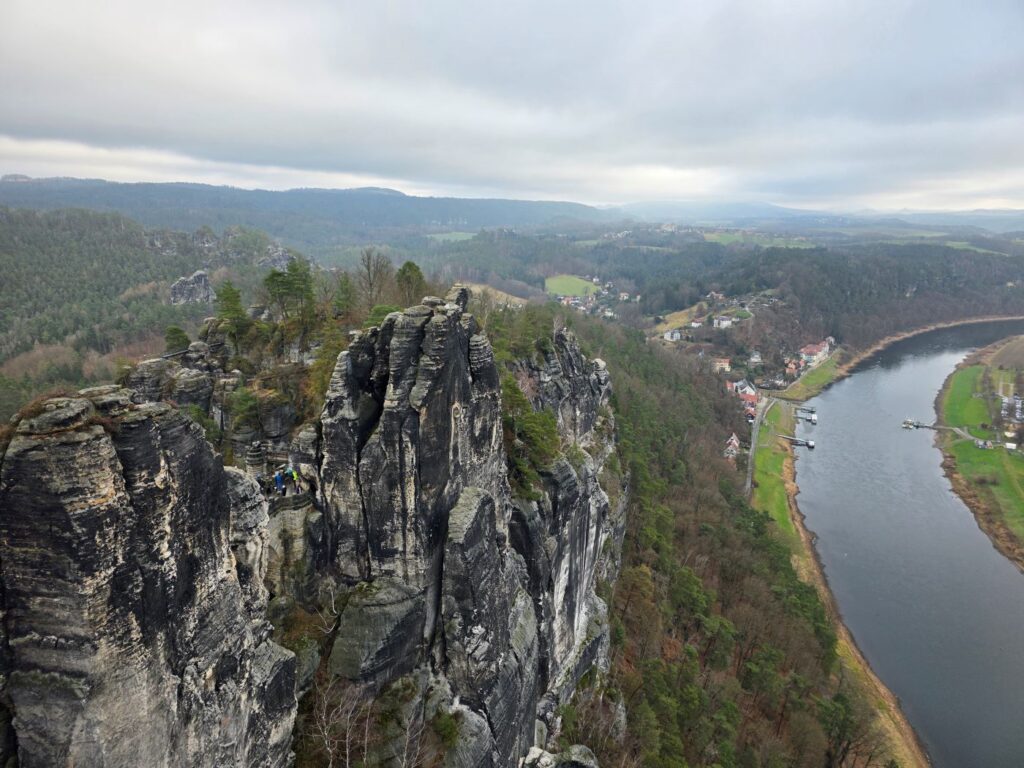 Silvester in Prag (04.01.2026) große, zerklüftete Felsformationen im Vordergrund und ein breiter Fluss, der sich durch eine bewaldete Hügellandschaft schlängelt, im Tal