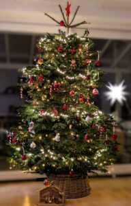 Ein festlich geschmückter Weihnachtsbaum mit bunten Lichtern, in einer Wohnung und davor eine kleine Grippe aus Holz
