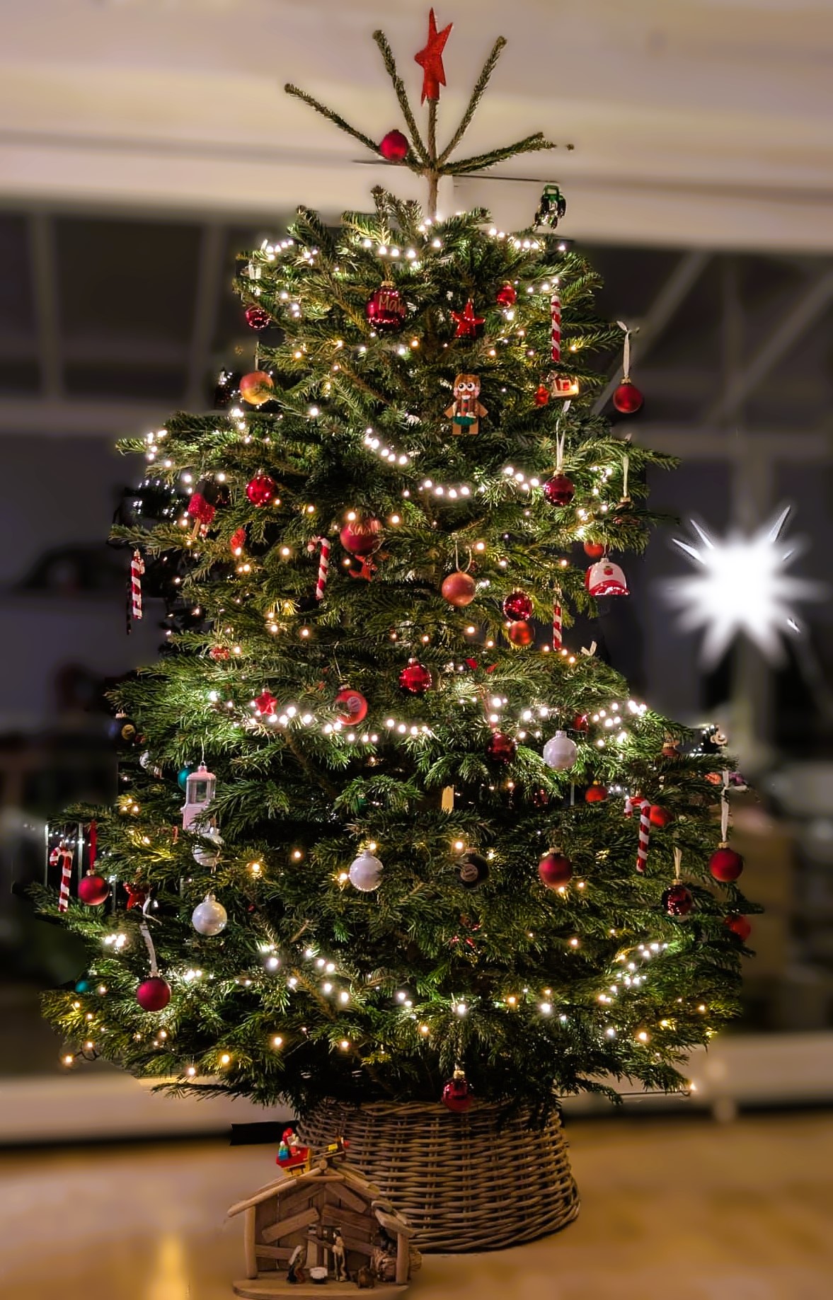 Ein festlich geschmückter Weihnachtsbaum mit bunten Lichtern, in einer Wohnung und davor eine kleine Grippe aus Holz