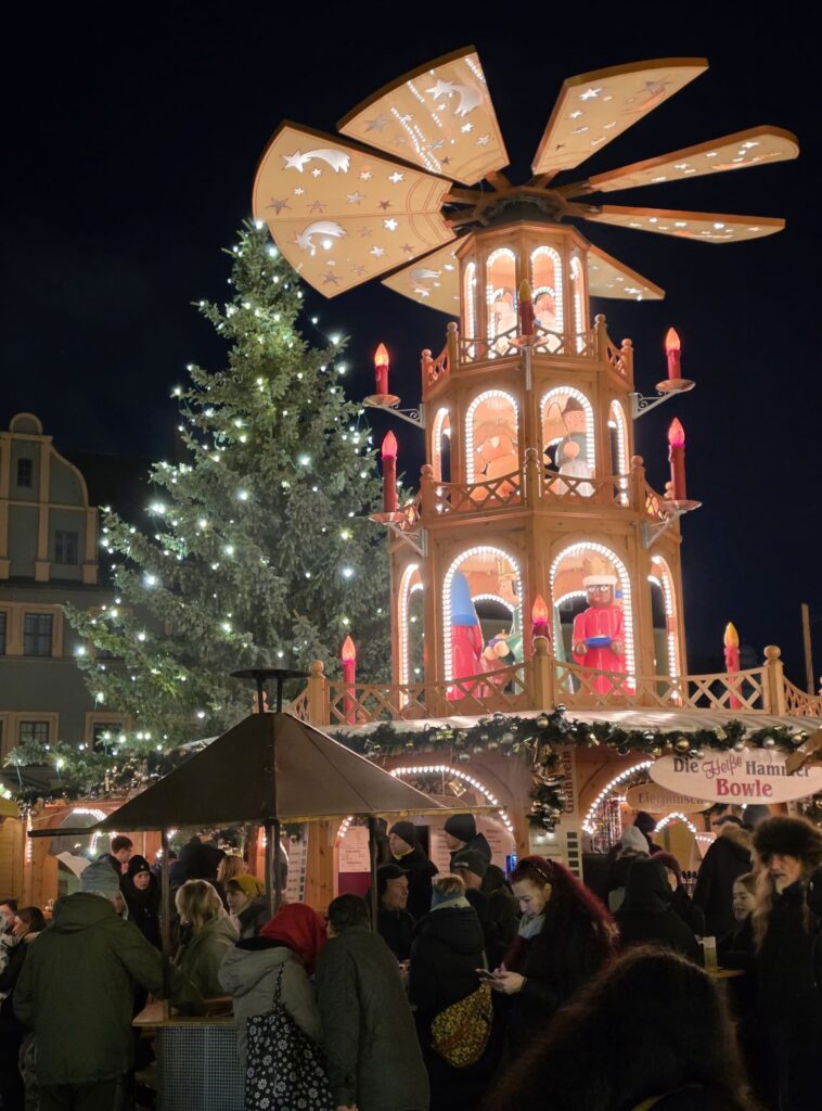 Silvester in Prag (04.01.2026) ein weihnachtlich beleuchteter Markt mit einer großen Holzpyramide, einem Weihnachtsbaum und vielen Menschen