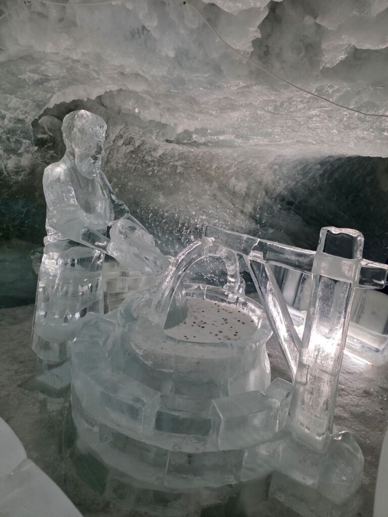 Glacier Express (01.02.2026) Eine Eissulptur in einer Eishöhle, die einen Mann vor einem Brunnen zeigt