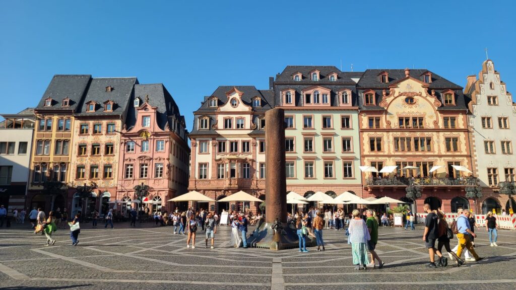 Stadtabenteuerspiel Mainz (13.02.2026) ein großer Platz in der Mainzer Innenstadt mit einer Säule im Mittelpunkt, vielen Menschen auf dem Platz und älteren Häusern im Hintergrund