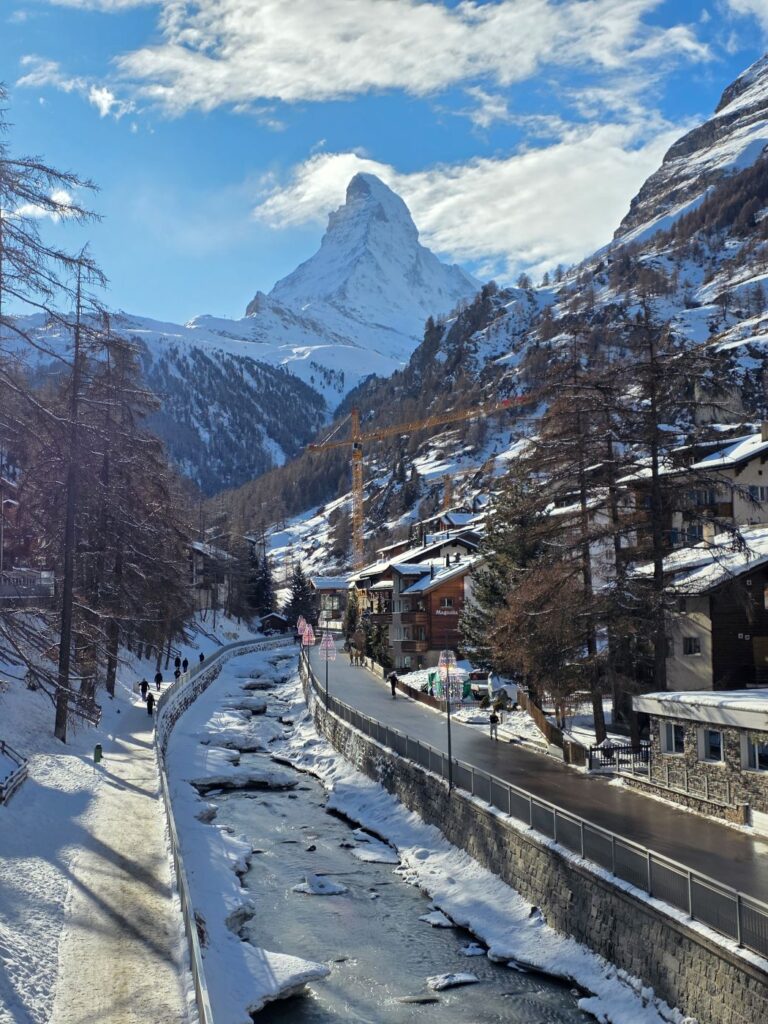 Glacier Express (01.02.2026) Blick über einen vereisten Fluß der an Zermatt vorbei fließt und im Hintergrund das verschneite Matterhorn
