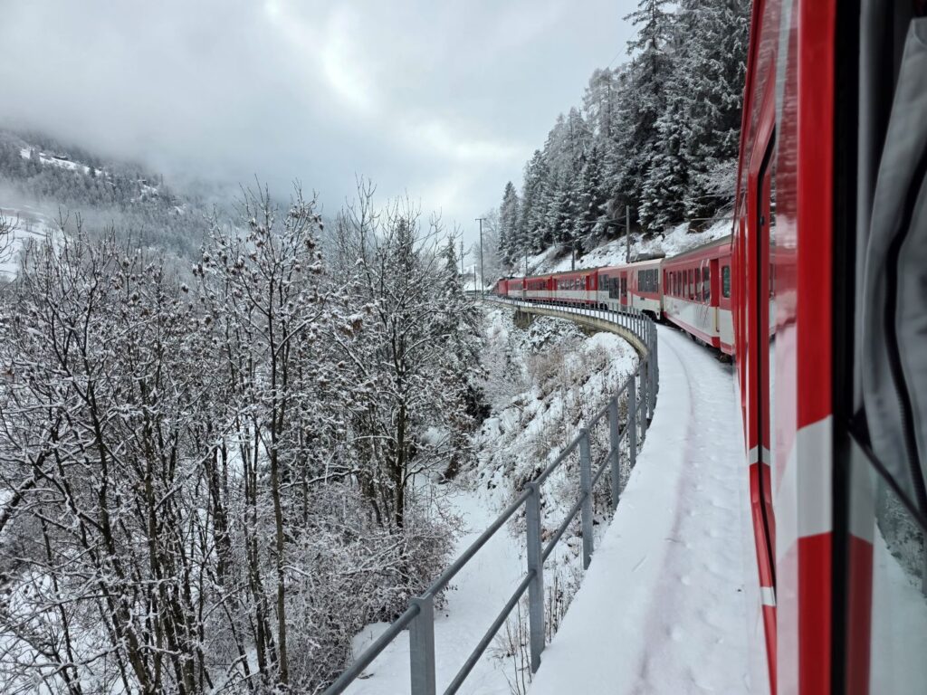 Glacier Express (01.02.2026) Blick aus einem Zugfenster seitlich auf den selbigen, der durch eine verschneite Winterlandschaft fährt