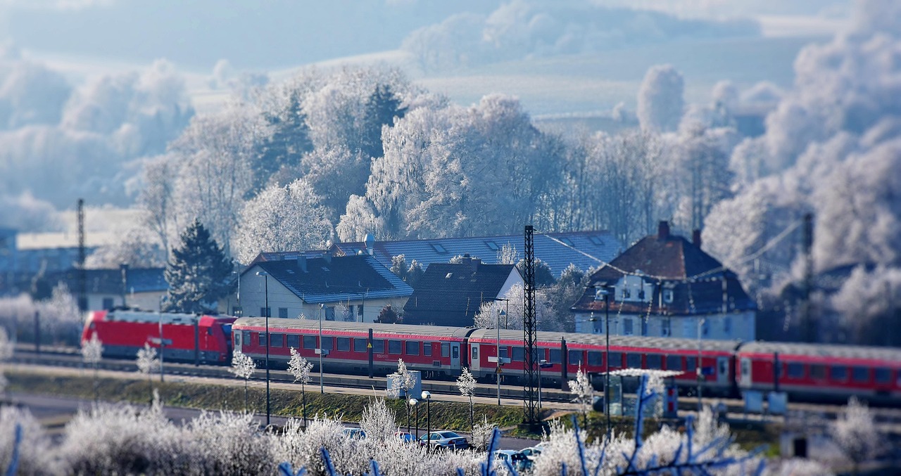 Glacier Express (01.02.2026) roter Zug der durch eine Winterlandschaft vorbei an Häusern fährt, im Hintergrund Bäume mit Reif